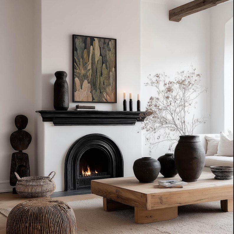 Textured botanical cactus poster in olive, beige, and cream tones, framed print above a black fireplace mantel in a cozy neutral living room with woven accents.