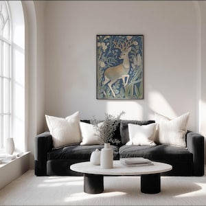 Intricate blue and cream stag illustration with botanical details wall art print hangs on a white wall above a black sofa in a bright living room.
