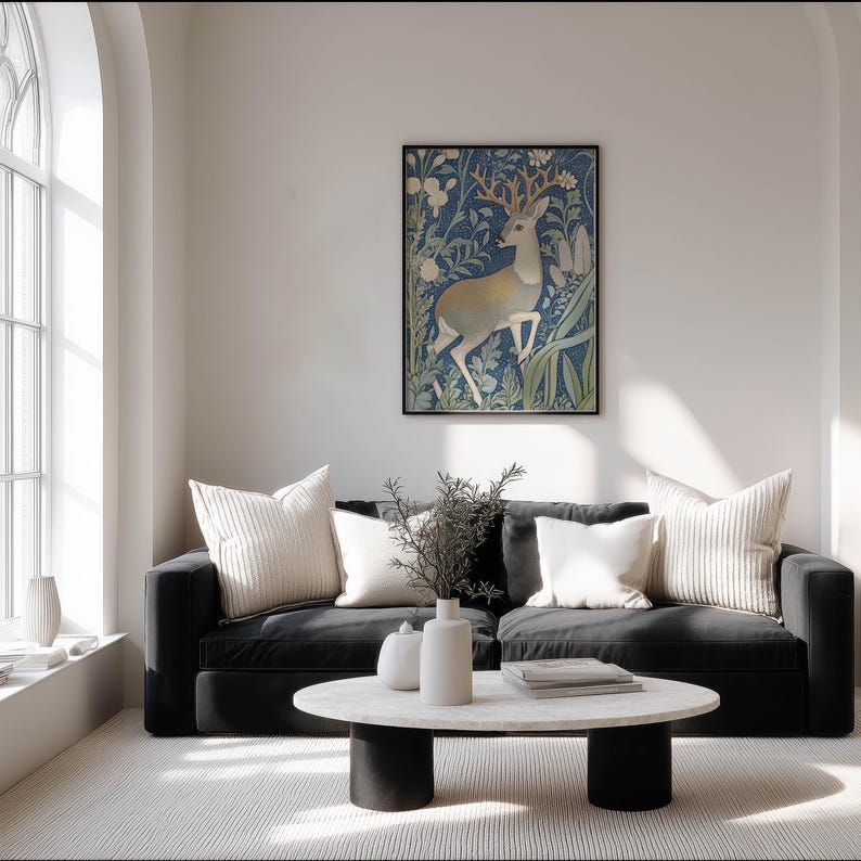 Intricate blue and cream stag illustration with botanical details wall art print hangs on a white wall above a black sofa in a bright living room.