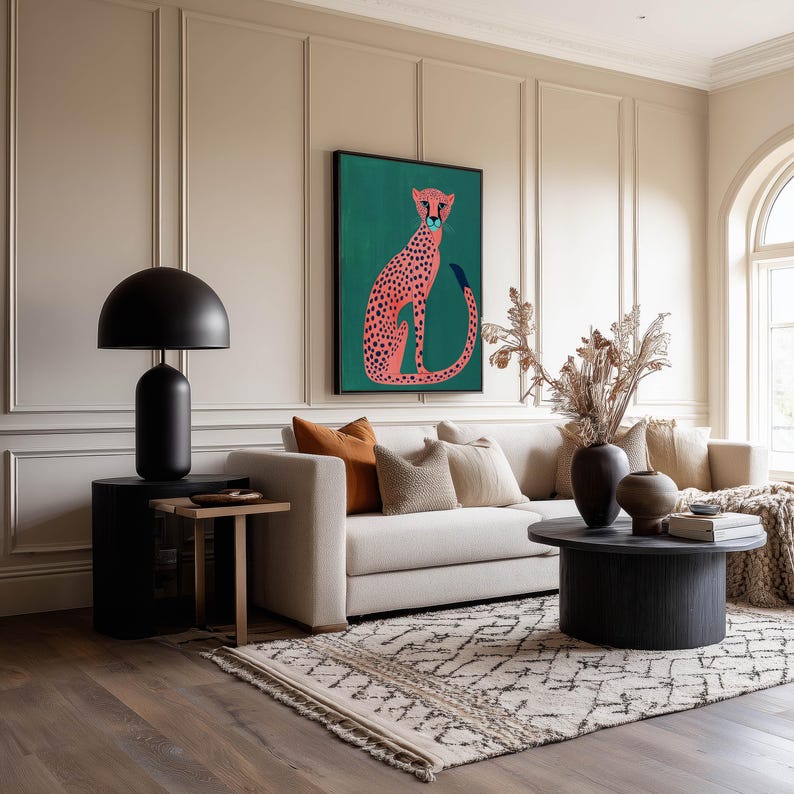 Illustrated art print of a pink spotted cheetah on a green background, framed above a beige sofa in a warm living room with paneled walls and earthy decorative vases.