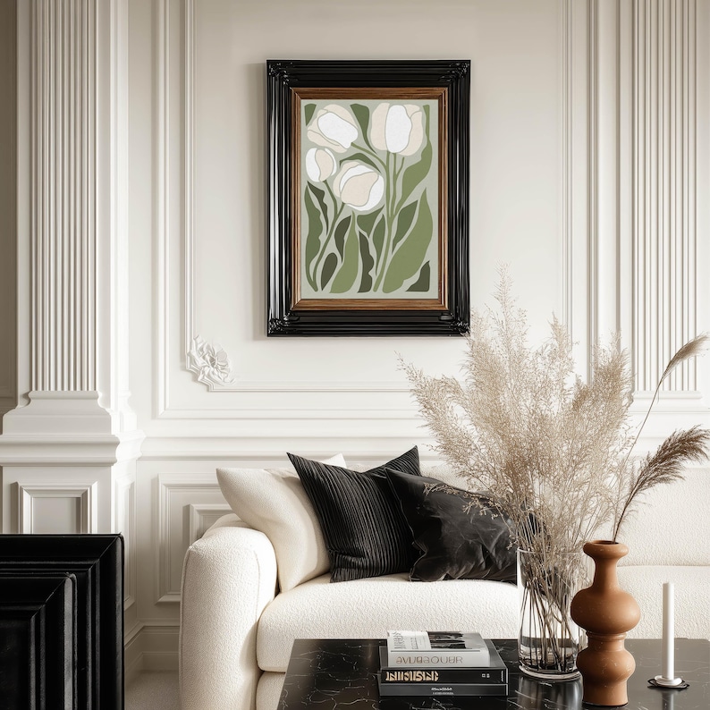 Classic botanical art print in muted greens and cream with a refined mood, framed in black and centered on an ornate paneled wall above a cream sofa styled with pampas grass.
