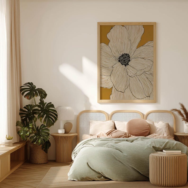 Elegant line-drawn flower in white over golden yellow, serene contemporary style, framed art print hanging above a cane headboard in a calm bedroom.