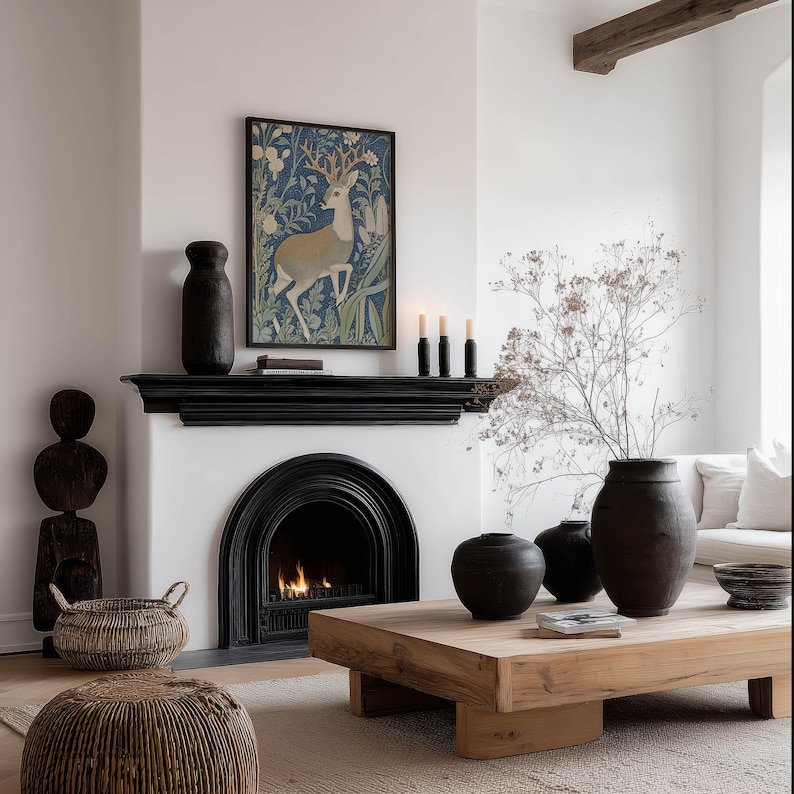 Vintage style blue botanical deer illustration wall art print is framed above a black fireplace mantel in a cozy neutral living room with a glowing fire.