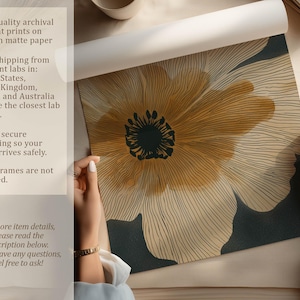 Close-up abstract flower art print in neutral beige and charcoal with golden details, clean modern style, shown being unrolled on a tabletop with paper info overlay.