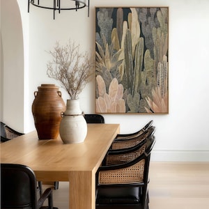 Layered botanical shapes in muted greens and beiges, framed art print above a light wood dining table with cane-back chairs and ceramic vases.