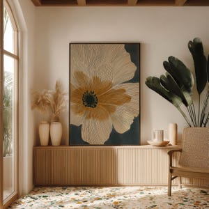 Neutral floral poster in cream and charcoal with an ochre center, minimalist and calming mood, centered above a low cabinet in a bright styled corner.