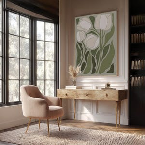 Bright modern floral art print in sage and ivory with a calm minimalist mood, large framed print above a rustic wooden desk in a bright home office with bookshelves and a blush lounge chair.