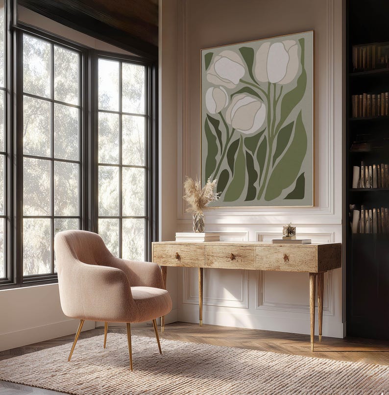 Bright modern floral art print in sage and ivory with a calm minimalist mood, large framed print above a rustic wooden desk in a bright home office with bookshelves and a blush lounge chair.