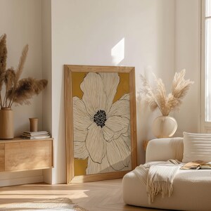 Minimal floral illustration with ivory petals and warm mustard backdrop, Scandinavian feel, framed poster leaning near a wood sideboard in an airy living room.