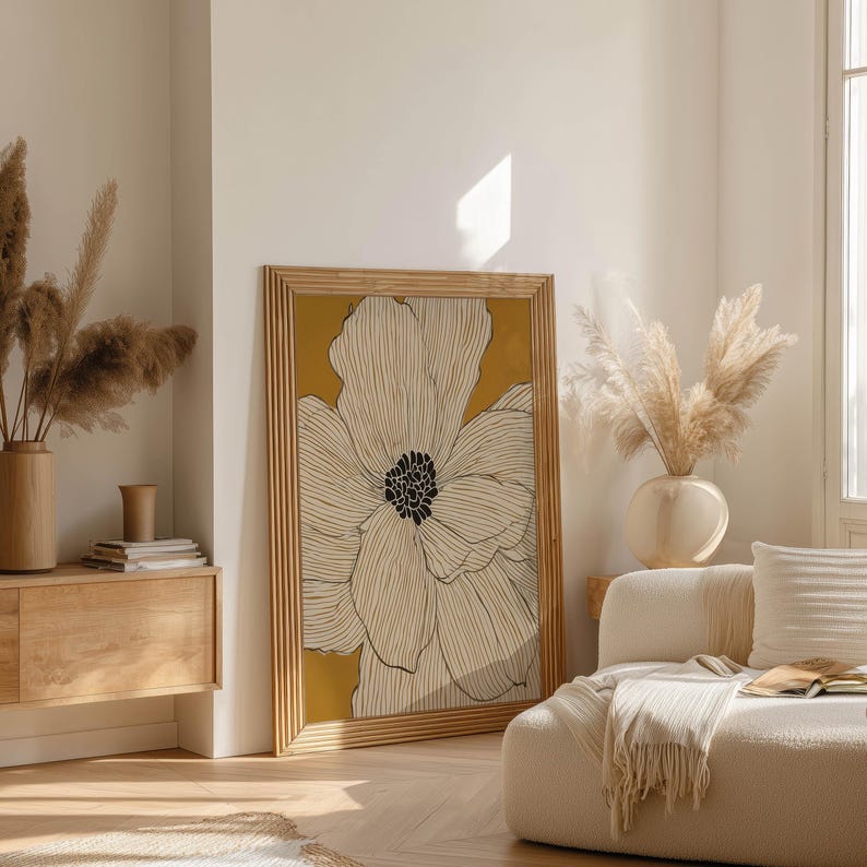 Minimal floral illustration with ivory petals and warm mustard backdrop, Scandinavian feel, framed poster leaning near a wood sideboard in an airy living room.