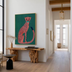 Playful wall art print showing a stylized pink cheetah with navy spots on teal, hanging above a sculptural live-edge wooden console in a modern hallway with pendant lights.
