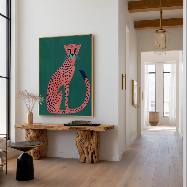 Playful wall art print showing a stylized pink cheetah with navy spots on teal, hanging above a sculptural live-edge wooden console in a modern hallway with pendant lights.
