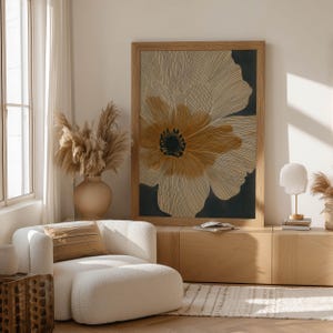 Graphic botanical wall art print featuring a single large bloom in cream and charcoal with golden petals, modern organic mood, leaning on a low cabinet with decor.