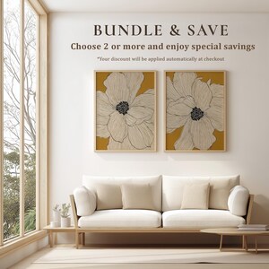 Coordinated matching set of two modern botanical flower posters in white and mustard yellow, a calm gallery wall pair displayed side by side above a sofa.