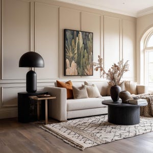 Botanical cactus scene in warm neutrals and dark background, framed art print hanging above a beige sofa with paneled walls and an earthy patterned rug.