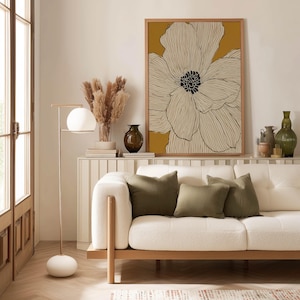 Contemporary line art flower in ivory and yellow with bold dark center, clean minimalist look, framed poster above a slim console shelf by a sofa.