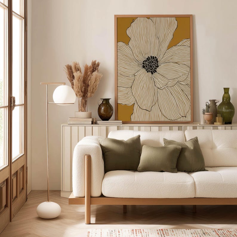 Contemporary line art flower in ivory and yellow with bold dark center, clean minimalist look, framed poster above a slim console shelf by a sofa.