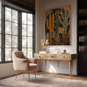 Large botanical art print with layered cactus shapes in mustard and teal, bright modern feel; framed art print above a rustic wooden desk in a bright home office with built-in bookshelves and a blush lounge chair.