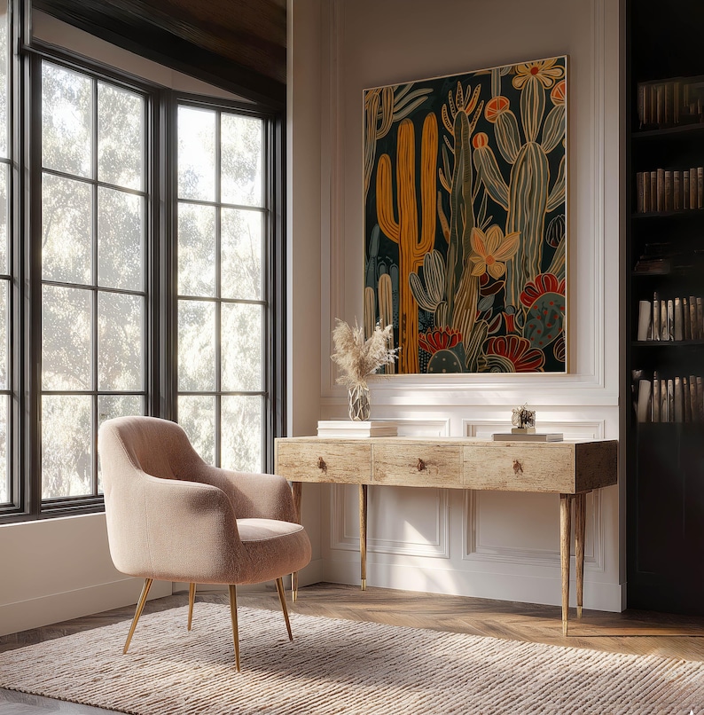 Large botanical art print with layered cactus shapes in mustard and teal, bright modern feel; framed art print above a rustic wooden desk in a bright home office with built-in bookshelves and a blush lounge chair.