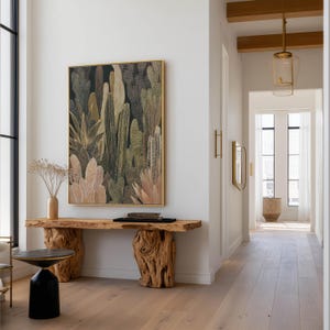 Detailed olive and tan cactus illustration with dotted highlights, physical art print hung above a live-edge wooden console in a modern hallway with glass pendant lights.