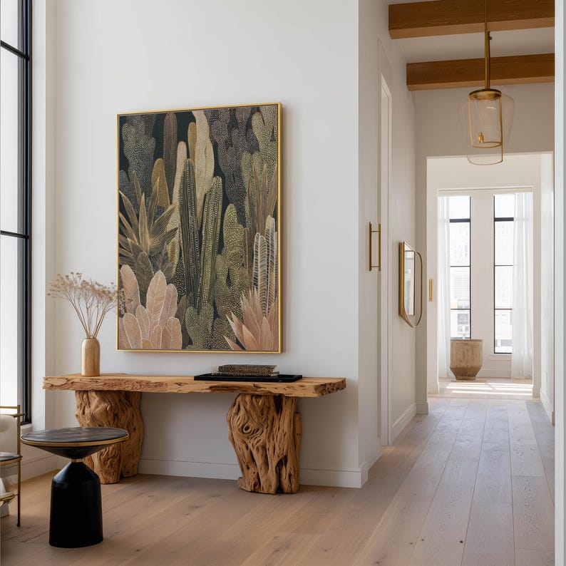Detailed olive and tan cactus illustration with dotted highlights, physical art print hung above a live-edge wooden console in a modern hallway with glass pendant lights.
