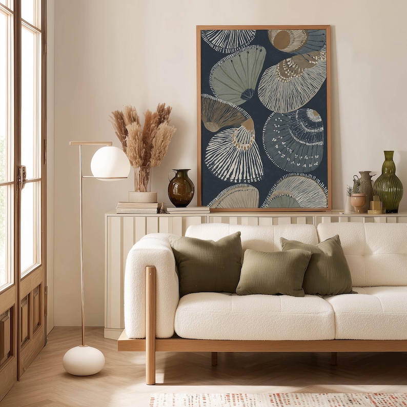 Minimalist seashell poster with graphic lines in blue and beige for a soothing coastal look, displayed above a slim console with ceramics and green cushions.