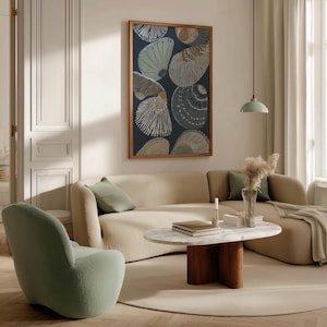 Patterned seashell art print in navy and sand tones with clean modern lines, hanging above a curved sofa with a round coffee table and stacked books.