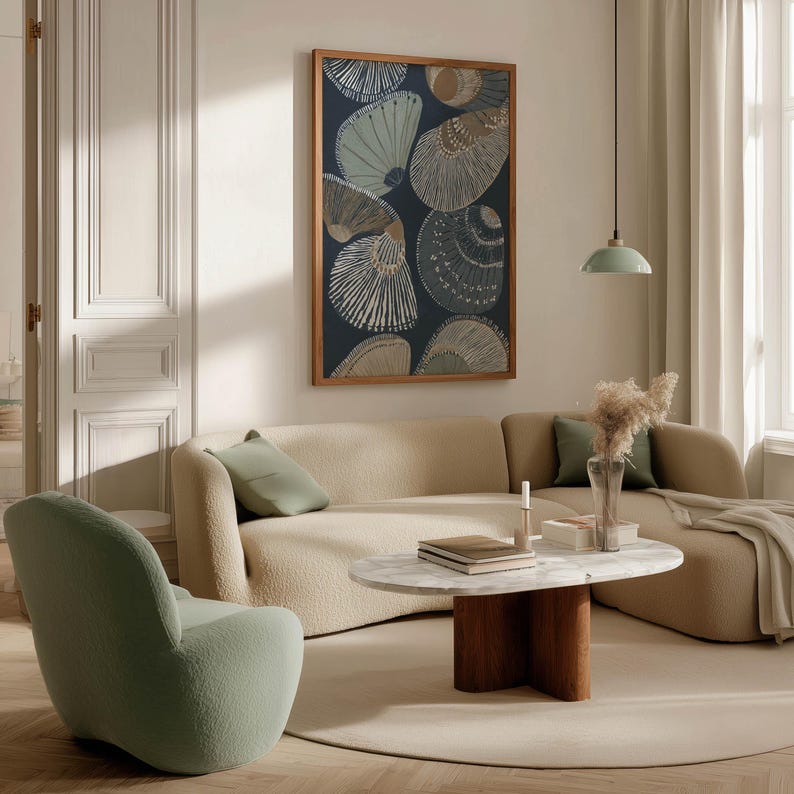 Patterned seashell art print in navy and sand tones with clean modern lines, hanging above a curved sofa with a round coffee table and stacked books.