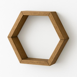 May include: A hexagonal wooden shelf in a warm brown tone. The shelf is mounted on a white wall, showcasing its geometric design. The shelf is made of wood and has a modern, minimalist aesthetic.