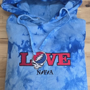 May include: A light blue tie-dye hoodie with a drawstring hood. The word "LOVE" is embroidered in red, with a skull and lightning bolt graphic. Below the word "LOVE" is the text "NFA".