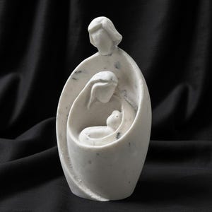 May include: A white marble sculpture depicting a family. The sculpture features a mother, father, and child in a nested design. The sculpture has dark gray speckles throughout and is set against a black background.