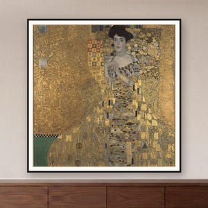 Könnte beinhalten: Ein quadratischer Kunstdruck im Rahmen zeigt das Porträt einer Person mit dunklem Haar, die ein Kleid mit komplexen goldenen, schwarzen und silbernen geometrischen Mustern trägt. Der Hintergrund ist eine texturierte, schimmernde Blattgoldfläche.