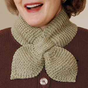 May include: A light green knitted scarf with a unique design that creates two pointed ends. The scarf is worn around the neck of a person.