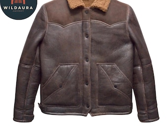 Puede incluir: Una chaqueta de cuero marrón oscuro con cuello de borreguito color canela, cierre frontal de botones y dos bolsillos delanteros grandes. La chaqueta tiene un canesú de estilo western en el pecho y los hombros. El logo WILDAURA JACKET es visible.