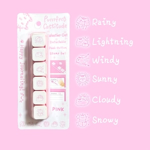 May include: A pink "Purrfect Cattitude" stamp set with six weather-themed stamps featuring cat illustrations. The stamps include "Rainy," "Lightning," "Windy," "Sunny," "Cloudy," and "Snowy." The set is packaged with the text "Happy Journaling!"