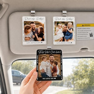 May include: Three personalized car visor ornaments with family photos. Two ornaments read "Drive safe, Daddy!" and the third says "Stay Safe! Come home!". Each features a photo, text, and a metal clip for attachment. The bottom ornament is held by a hand.