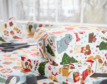 May include: Christmas-themed gift wrap featuring a repeating pattern of cartoon dogs, Christmas trees, and snowflakes on a white background. The image shows wrapped gifts, wrapping paper rolls, and scissors.