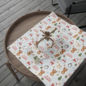 Puede incluir: Un regalo envuelto y papel de regalo con un patrón repetido de osos polares, renos, pingüinos y árboles de Navidad. Las palabras "My First Christmas" están impresas en el papel. También se ven una cinta marrón y unas tijeras.