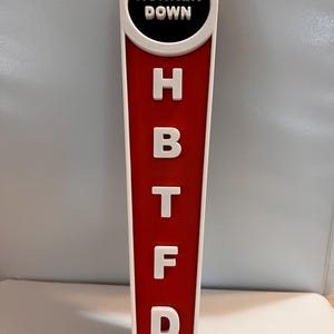 Puede incluir: Un tirador de grifo rojo y blanco con la frase "HUNKER DOWN" en blanco sobre un fondo negro. Debajo, las letras blancas H, B, T, F y D se muestran sobre un fondo rojo.