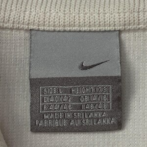 以下が含まれることがあります： 白の衣服に縫い付けられた灰色のナイキタグのクローズアップ。タグにはナイキのスウッシュロゴと、サイズ、高さ、測定値を含むテキストがあります。タグには「Made in Sri Lanka」と「Fabriqu&eacute; au Sri Lanka」と書かれています。