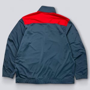 May include: A teal and red track jacket. The jacket has a red panel across the shoulders and upper back, with a teal body and sleeves. It features a stand-up collar and a full-length zipper.