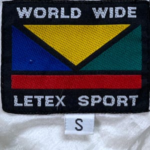 May include: Black rectangular patch with the words "WORLD WIDE" above a colorful geometric design. Below the design is the text "LETEX SPORT". A small white tag with the letter "S" is below.