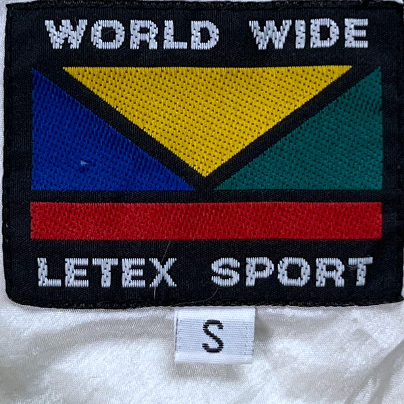 May include: Black rectangular patch with the words "WORLD WIDE" above a colorful geometric design. Below the design is the text "LETEX SPORT". A small white tag with the letter "S" is below.