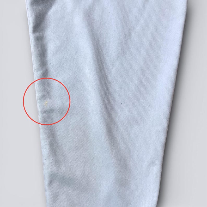 May include: Close-up of a light blue fabric, possibly clothing. The fabric has a subtle texture and a few small yellow spots. The image is well-lit, highlighting the details of the material.