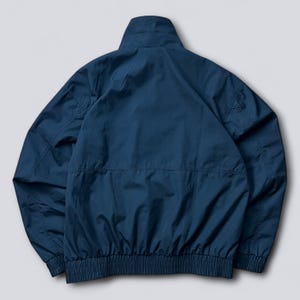 May include: A navy blue jacket with a high collar and a ribbed hem. The jacket has a zipper closure and two pockets. The back of the jacket is visible, showing the seams and the overall shape.