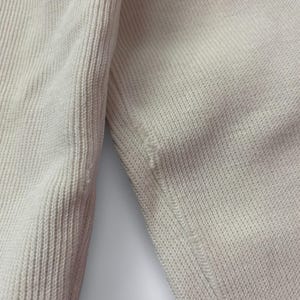 以下が含まれることがあります： クリーム色のニット生地のクローズアップ。質感と縫い目の詳細を示しています。生地はセーターまたは同様の衣服のもので、縫い目と一部の畝模様が見えます。
