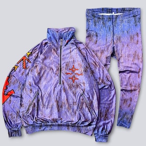 May include: A two-piece athletic set in shades of purple, blue, and brown. The jacket has a half-zip, pockets, and graphic designs in red, yellow, and black. The matching leggings complete the set. The fabric has a metallic sheen.