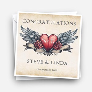 May include: A square greeting card with a vintage design. The card features the word "CONGRATULATIONS" at the top, with a red heart in the center, adorned with wings and roses. The names "STEVE & LINDA" and the date "26th October 2025" are also displayed.