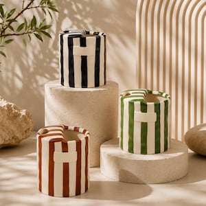 Puede incluir: Tres macetas de cerámica con rayas verticales en blanco y negro, verde y blanco, y marrón y blanco. Cada maceta tiene un asa rectangular y se apoya sobre un pedestal de hormigón. Las macetas son decorativas.