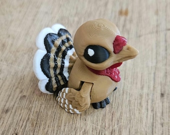 May include: A 3D-printed turkey figurine. It has a tan body, a red wattle, and a black and white eye. The turkey has a detailed tail with white, black, and brown feathers. The figurine is on a wooden surface.